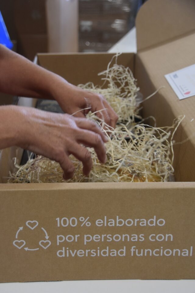 Imagen. Primer plano de unas manos trabajando en la preparación de uno de los lotes de Navidad para empresas de más de 50 trabajadores del proyecto 'Dale Valor Social' que ha impulsado la Fundación AltoAragón Integración (FAI) a través de Somontano Social, su Centro Especial de Empleo.