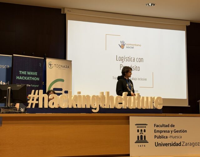 Imagen. A la izquierda, un estudiante presenta el proyecto elaborado para el reto propuesto por Somontano Social en el Hackathon The Wave Huesca 2026.