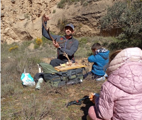 Imagen. Dos niños de espaldas en primer término y al fondo, el guía David tiene en sus manos una cornamenta de cérvido, en la jornada de senderismo interpretativo en Artasona, organizada por Somontano Social, el Centro Especial de Empleo de la Fundación AltoAragón Integración (FAI).