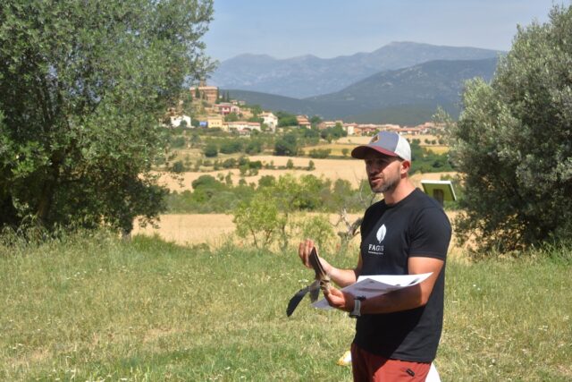 Imagen. David, de Fagus, con unas plumas de buitre en las manos durante su explicación. Al fondo, la iglesia de Santiago Apóstol de Bierge.