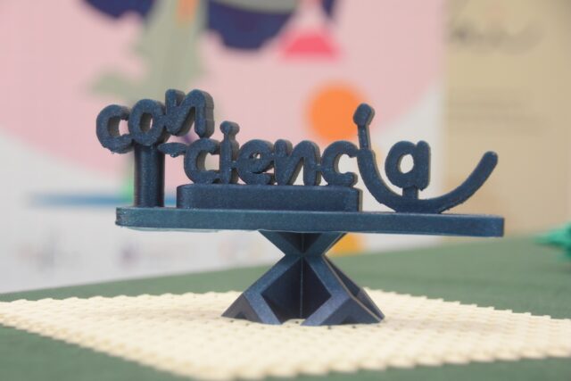 Imagen. Fotografía del logotipo del proyecto Con-Ciencia realizado con filamento azul en la impresora 3D en las instalaciones de Somontano Social, el Centro Especial de Empleo de la Fundación AltoAragón Integración (FAI).