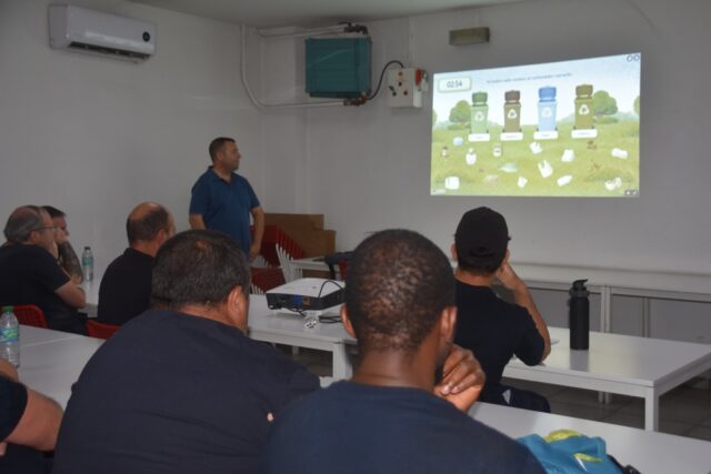 Imagen. De espaldas, grupo de trabajadores del Centro Logístico de Somontano Social atienden a las explicaciones en el Taller de Reciclaje y gestión de residuos.
